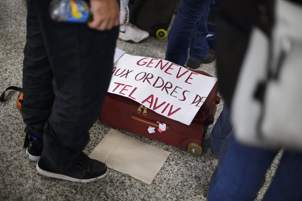 Pro-Palestinian activists stand next to a placard reading "Geneva, gets orders from Israel" as they protest at Geneva airport on April 15, 2012 in Geneva. Several dozen pro-Palestinian activists protested at Geneva airport, saying authorities prevented them from boarding a Tel Aviv-bound flight as part of a "fly-in" that Israel has vowed to block.    AFP PHOTO/ FABRICE COFFRINI